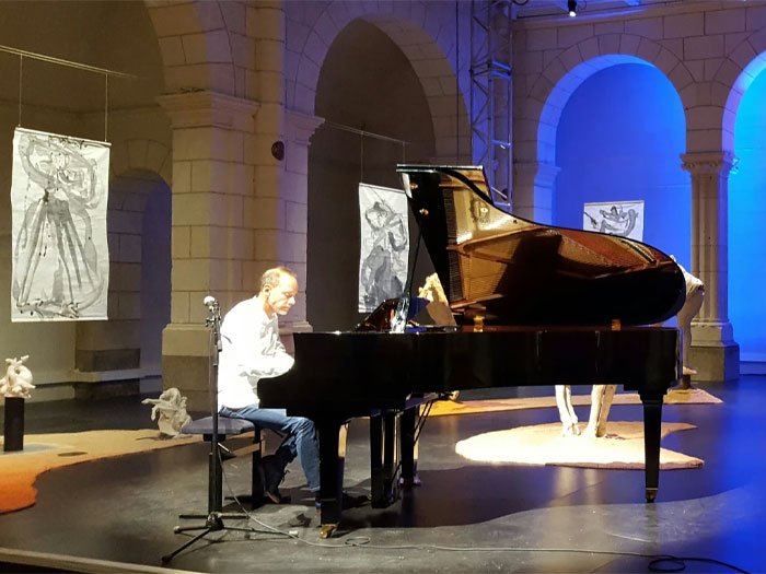 Yann Crépin, en pleine performance, joue du piano sur une scène éclairée, entouré d'œuvres d'art, exprimant sa connexion profonde avec son intuition artistique.