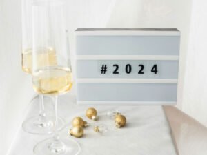 Deux coupes de champagne sur une table élégante avec une boîte lumineuse affichant '#2024', accompagnées de décorations dorées, symbolisant l'accueil festif de la nouvelle année et l'engagement envers une transformation positive.