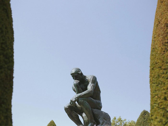 La statue en bronze "Le Penseur" de Rodin, captée dans un jardin tranquille, symbolise la profonde réflexion humaine, rappelant l'importance de la pensée soulignée dans l'article sur la dignité et les capacités de réflexion de l'homme.