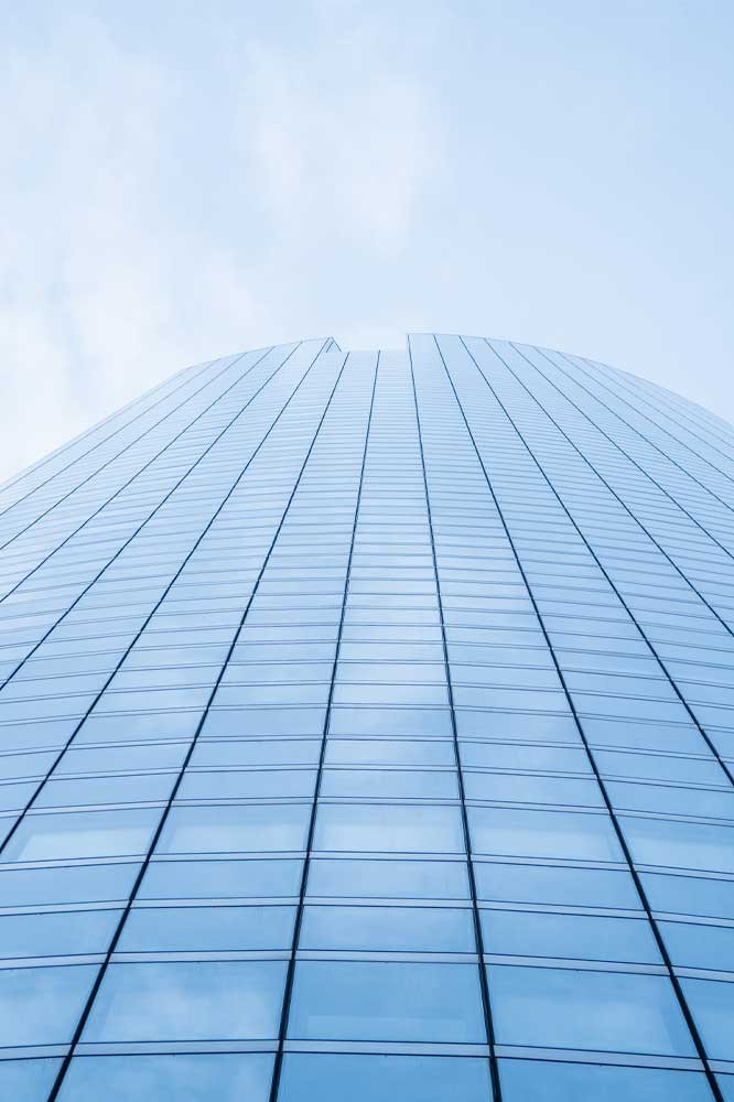 Vue verticale d'un gratte-ciel moderne avec un design épuré de verre bleuté, représentant la catégorie 'Vie des affaires' sur le blog de Kris Saint Ange. Cet immeuble symbolise la montée vers le leadership et l'innovation en entreprise, des thèmes clés abordés dans les articles de cette section.