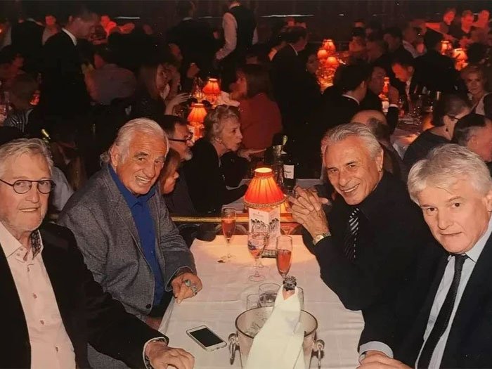 Quatre hommes souriants, dont Michel Berreur, assis autour d'une table lors d'un événement mondain, reflétant une atmosphère chaleureuse et conviviale, symbolisant les liens et les rencontres enrichissantes dans le monde du spectacle.